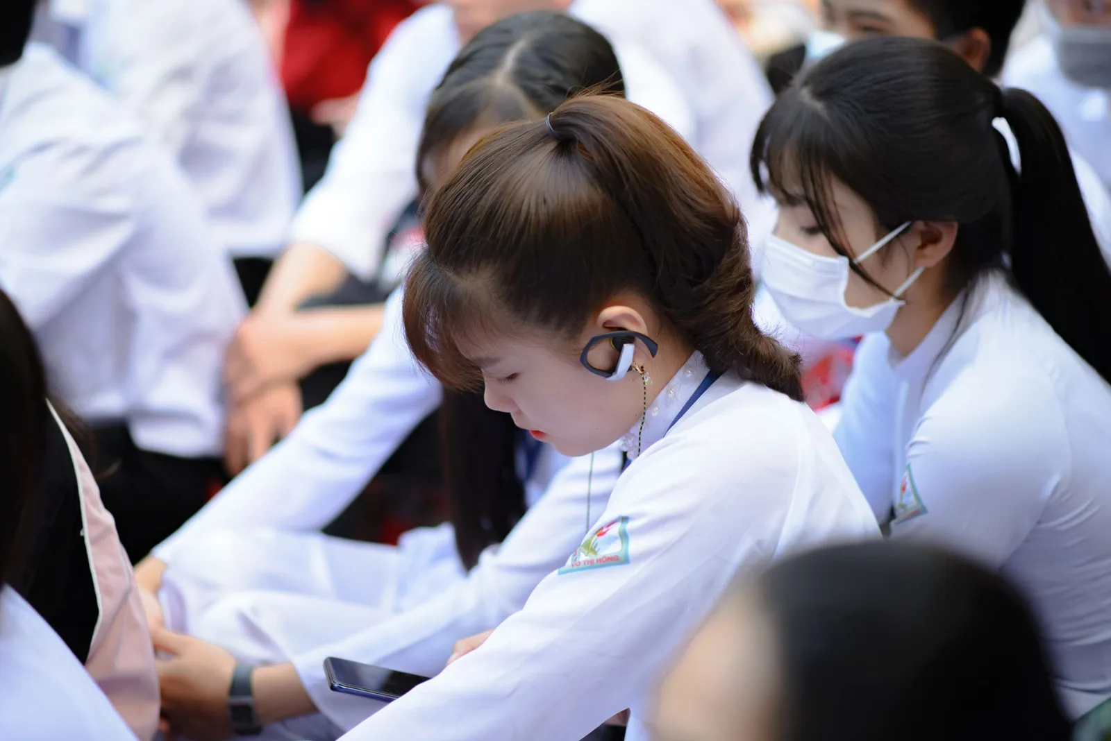 Group of Asian students in uniforms using smartphones and earphones indoors.