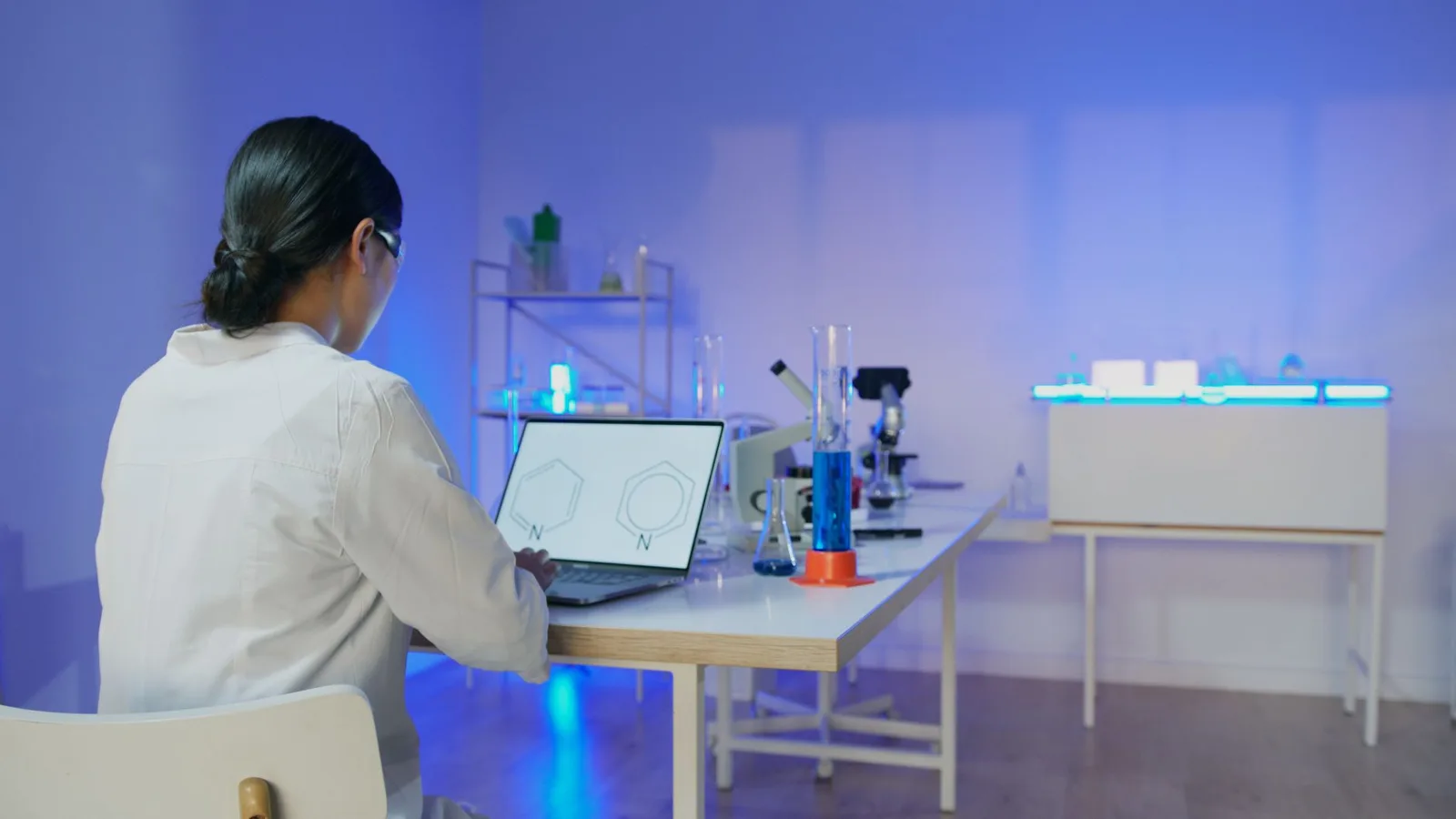 Female scientist studying chemical structures on a laptop in a modern laboratory setting.