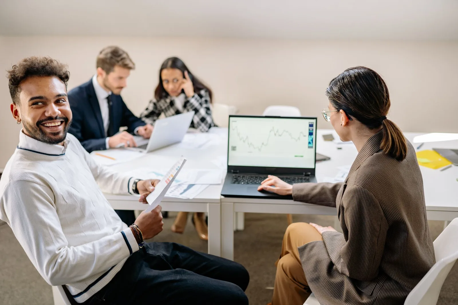 A group of professionals engaged in a collaborative meeting with charts and technology in a modern office setting.