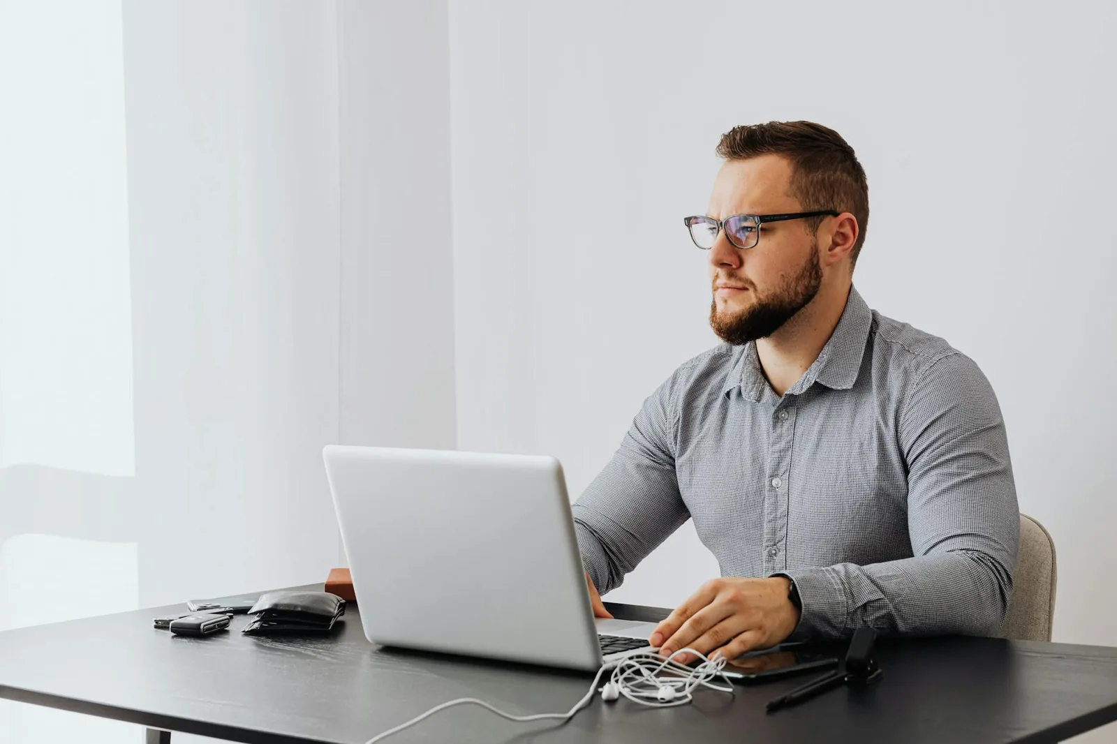 Bearded man with eyeglasses working on a laptop in a minimalist office setting.